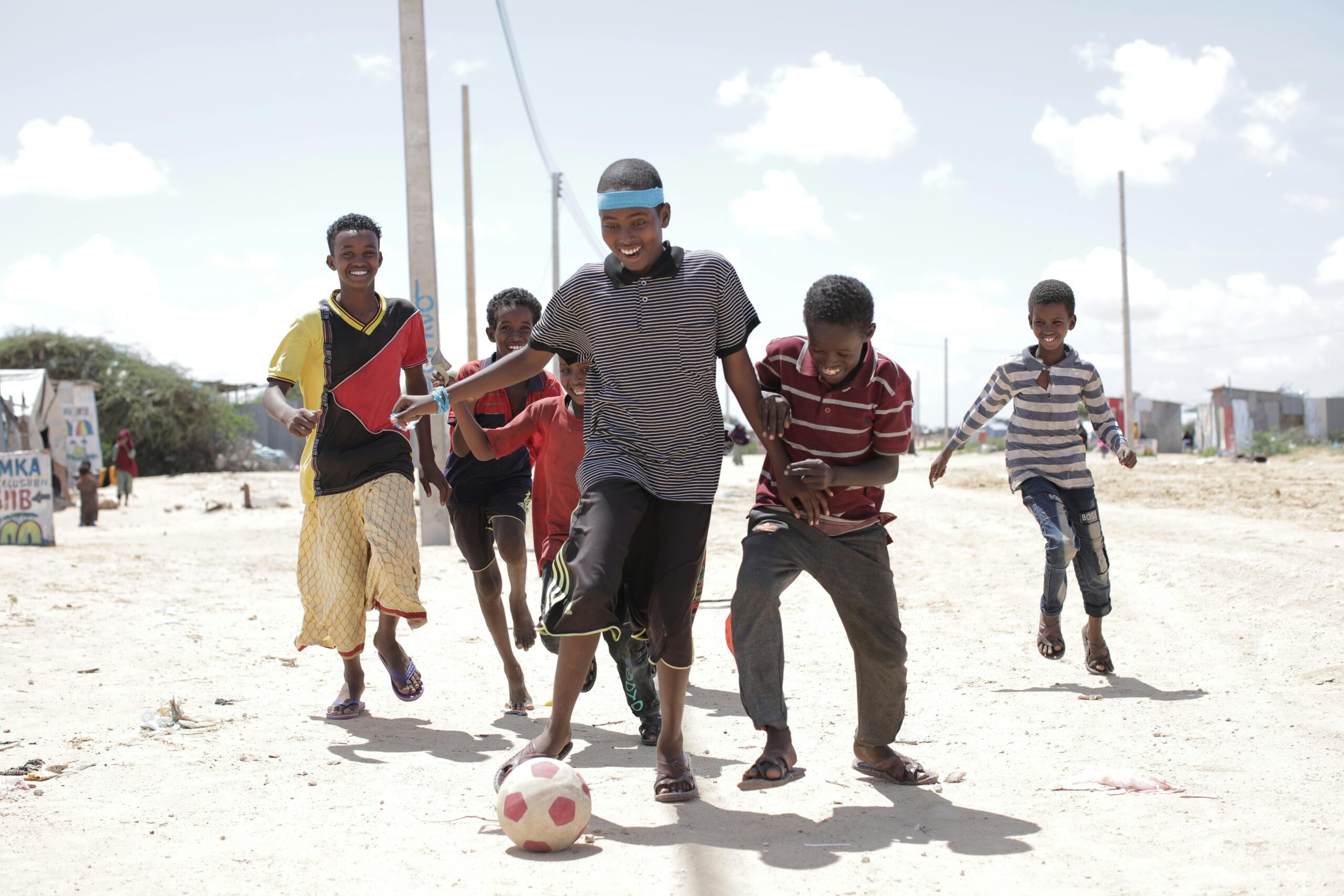 A group of Somali children playing soccer on a sunny day, showcasing joy and friendship.